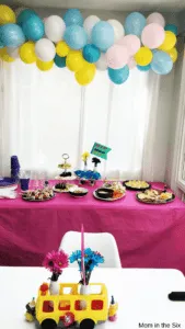 Balloon banner above table with food and Little People Bus center piece